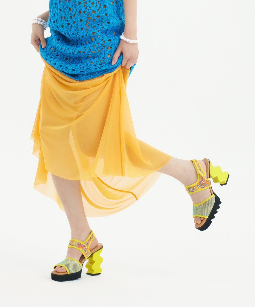 Person wearing a blue top and yellow skirt with colorful sandal platform heel on a white background